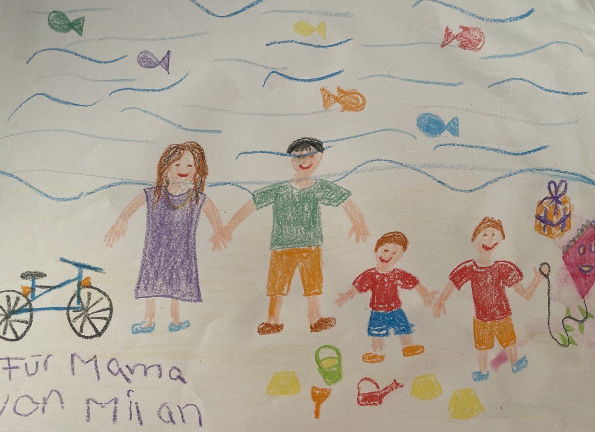 Dečji crtež: porodica ruku pod ruku na plaži, sa ribicama, biciklom i zmajem; u uglu rukom piše &bdquo;Für Mama von Milan&ldquo; – Za mamu, od Milana